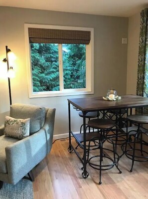 Ein Essbereich mit Tisch und Stühlen, ein Fenster mit Blick auf Bäume und eine Lampe.
