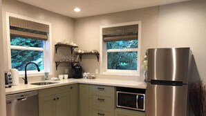 Una cocina moderna con armarios verdes, un refrigerador de acero inoxidable, un horno empotrado y una ventana con vistas a árboles.