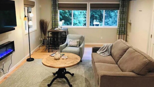 Una sala de estar con un sofá, una mesa de centro, un televisor y una ventana con cortinas.