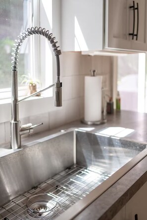 A modern kitchen with a stainless steel sink, a flexible faucet, and a window providing natural light. - Dog Friendly • Hot Tub • Firepit • Wine Country (Fennville)
