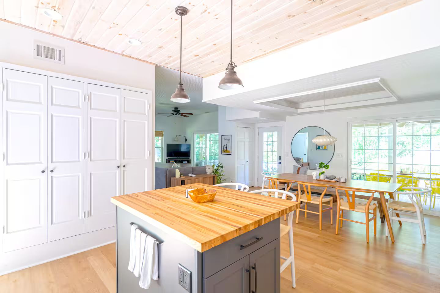 A modern kitchen with a wooden island, white cabinetry, and a dining area with a round table and chairs.