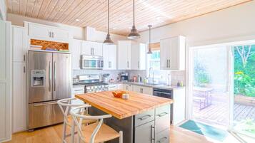 A modern kitchen with white cabinets, stainless steel appliances, a wooden island, and a view of the garden through a sliding glass door.