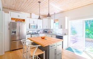 A modern kitchen with white cabinets, stainless steel appliances, a wooden island, and a view of the garden through a sliding glass door. - Private Hot Tub • Fenced Yard • Dog-Friendly Wine Country Retreat (Fennville)
