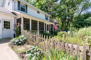 A two-story house with a covered porch, a wooden fence, and a garden with various plants. - Private Hot Tub • Fenced Yard • Dog-Friendly Wine Country Retreat (Fennville)