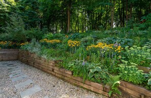 A garden with a stone pathway, wooden raised beds, and a variety of plants and flowers. - Dog Friendly • Hot Tub • Firepit • Wine Country (Fennville)