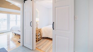 Ett sovrum med en stor skjutdörr, en säng, ett sängbord med en lampa och utsikt över staden genom stora fönster.