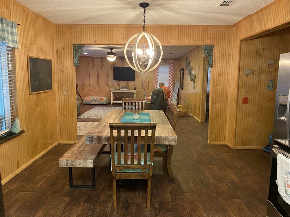 Un interior de madera con una mesa de comedor, sillas, un ventilador de techo y un refrigerador.
