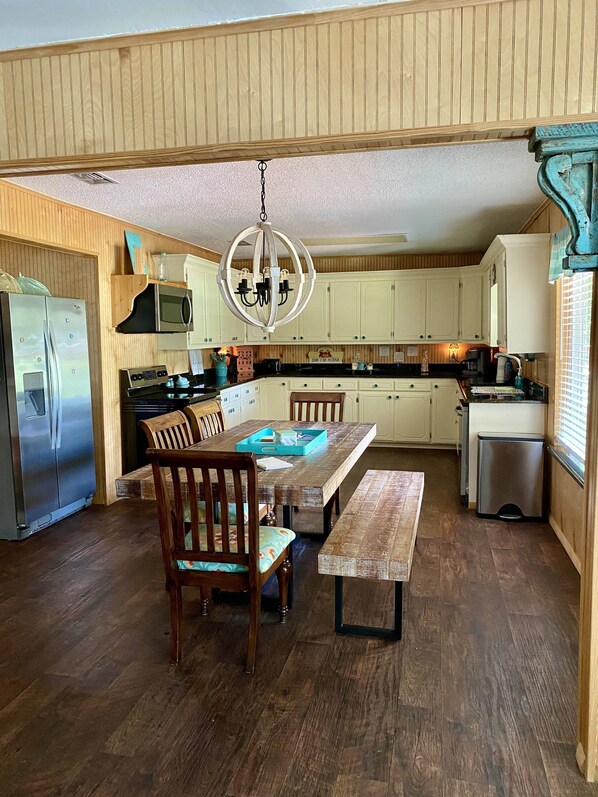 A kitchen with wooden cabinets, a stainless steel refrigerator, a microwave, a stove, and a dining table with chairs.