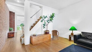 A modern living room with a staircase, a potted plant, a black leather sofa, and a small table with a lamp. - Gorgeous two story private home and garden 1/2 a block from McGolrick Park  (Brooklyn)