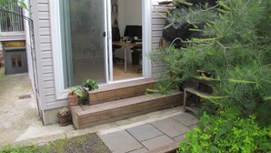 A house with a sliding glass door leading to a room with a desk and chair. There are steps leading to the door, and a small garden area with potted plants. - Gorgeous two story private home and garden 1/2 a block from McGolrick Park  (Brooklyn)