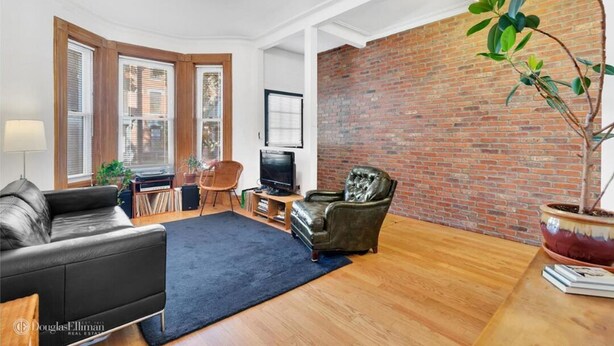 A living room with a brick wall, a black leather sofa, a wooden coffee table, and a potted plant. - Gorgeous two story private home and garden 1/2 a block from McGolrick Park  (Brooklyn)