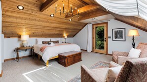 Une chambre avec un plafond en bois, un grand lit, une table de chevet, une chaise et une porte donnant sur un balcon.