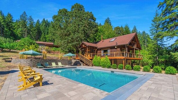 Une cabane en bois avec une piscine, entourée d’arbres et dotée d’une terrasse en pierre.