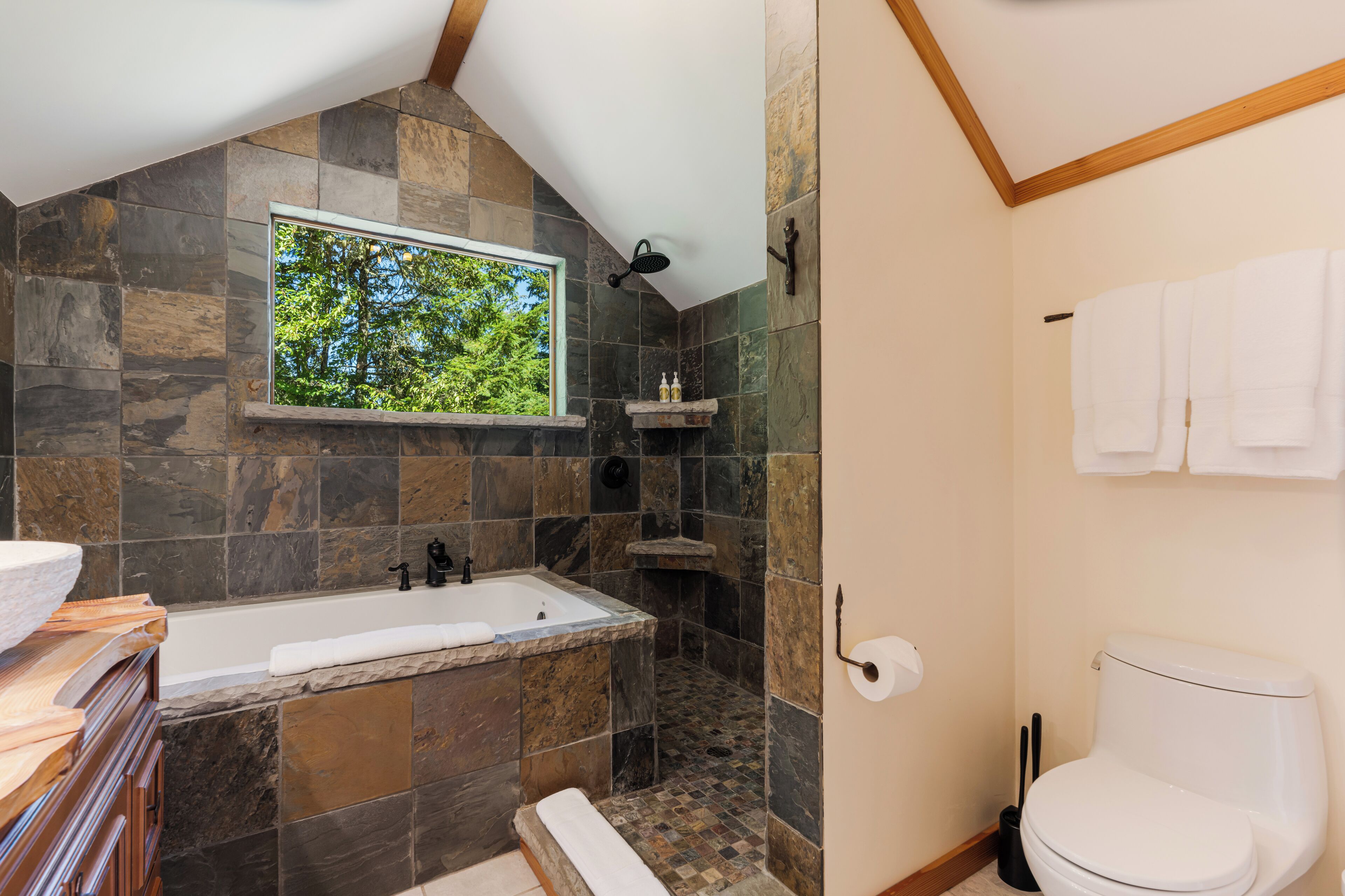 A bathroom with a stone shower, a bathtub, and a toilet.