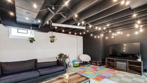 Ein modernes Wohnzimmer mit einer dunkelgrauen Ledersofa, einem Holztisch, einer bunten Spielmatte und einem Flachbildfernseher.