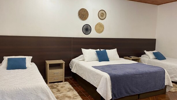 Habitación de hotel con dos camas, cabecero de madera, mesita de noche pequeña y un adorno en la pared.