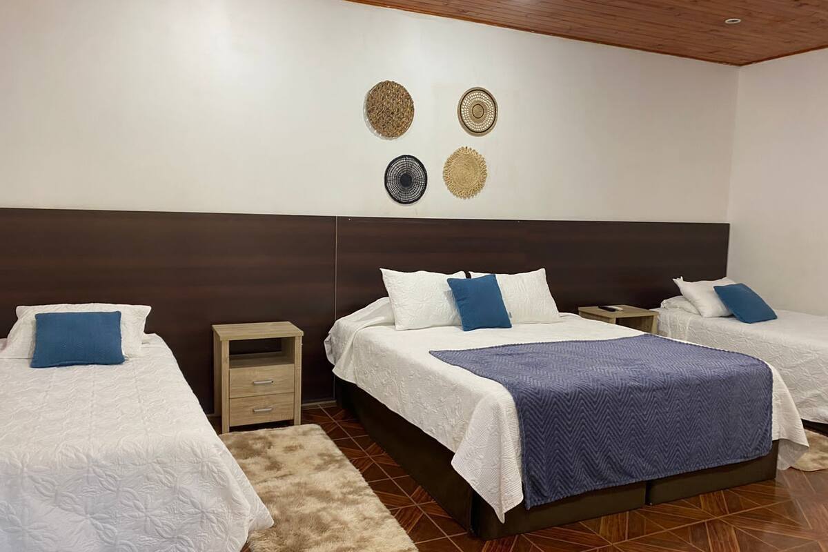 A hotel room with two beds, a wooden headboard, a small bedside table, and a decorative wall hanging.