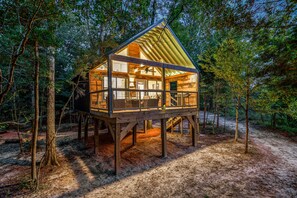 A wooden cabin with a glass enclosure, elevated on stilts, surrounded by trees. - Whiskey on the River (Petal)