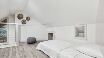 Quarto com teto inclinado, uma cama, janela com persianas e um pequeno espelho fixado na parede.