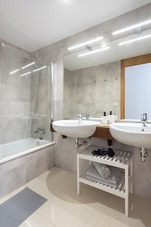 Un baño moderno con ducha envuelta en vidrio, dos lavamanos y un mueble de tocador con espejo.