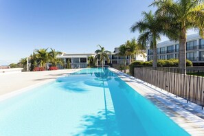 Una piscina con superficie de agua azul cristalina, rodeada por una terraza de baldosas blancas y una valla de metal negro.