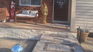 A house with a brick facade, a front porch with a bench, a large decorative door wreath, and a small statue. - Private, Quiet 1 Bedroom in Amityville (Amityville)