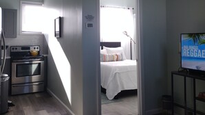 A compact hotel room with a kitchenette, a bed with a white comforter, a television, and a view of the outside through a window. - Private, Quiet 1 Bedroom in Amityville (Amityville)