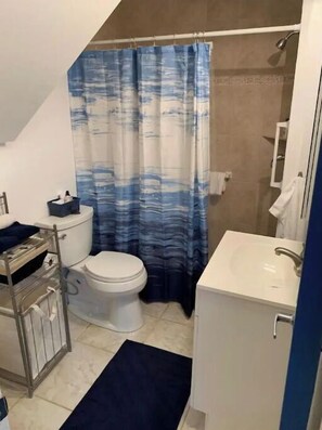 Un bagno con il water, un lavandino, una doccia e una tenda da doccia azzurra e bianca con motivo decorativo.