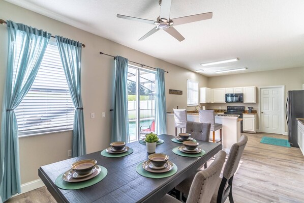 A dining area with a table set for four, a ceiling fan, and a view of the backyard through a sliding glass door. - 185 Windwood Bay (Davenport)