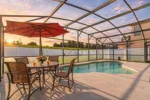 A covered outdoor area with a pool, a table with chairs, and a red umbrella.