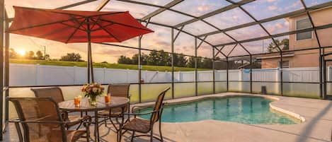 A covered outdoor area with a pool, a table with chairs, and a red umbrella.