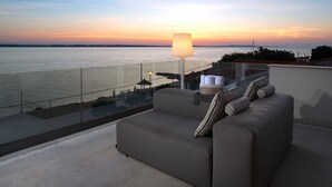 Ein Balkon mit einer Couch und einer Lampe, mit Blick auf ein Gewässer bei Sonnenuntergang.
