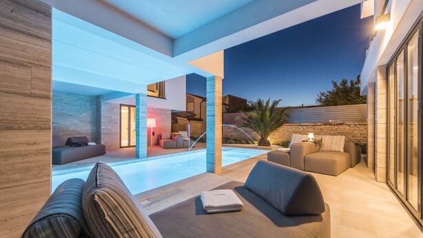 Ein moderner Außenbereich mit Pool, Sitzgelegenheiten und einer Steinmauer.