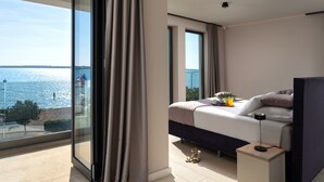 Ein modernes Schlafzimmer mit großem Fenster, einem Bett, einem Nachttisch und Blick aufs Meer.