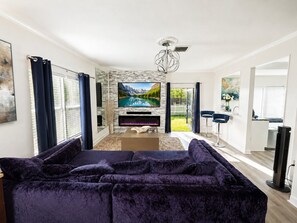 A modern living room with a large flat-screen TV, a fireplace, a sofa, and a dining area with bar stools. - Modern & Spacious Tampa Home 3bed 2bath + backyard Lanai. Great location! (Tampa)