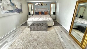 Une chambre à coucher avec un grand lit, deux tables de chevet, un lustre, un miroir et un tableau accroché au mur.
