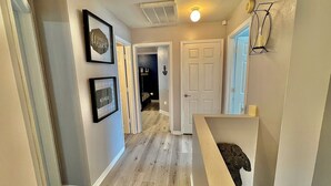 Un couloir avec un plancher en bois, une porte blanche et des tableaux encadrés accrochés au mur.