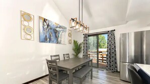 Une cuisine moderne avec une table à manger, des chaises, un réfrigérateur et un luminaire suspendu.