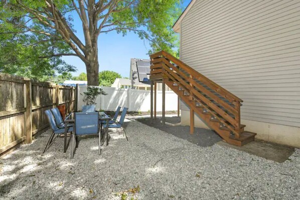 A backyard with a wooden staircase, a table with chairs, and a tree.