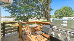 Une terrasse en bois avec un barbecue et des chaises en métal.