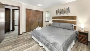 Une chambre à coucher avec un grand lit, une tête de lit en bois, une table de chevet avec une lampe et une œuvre d’art accrochée au mur.