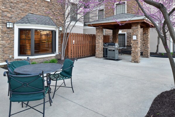 A backyard with a stone patio, a grill, and a wooden fence. - Cozy Suite | Free Breakfast + Pool (Plainfield)