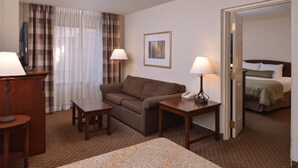 Una habitació d'hotel amb un sofà marró, dues taules petites, un llit, un telèfon i un quadre a la paret.