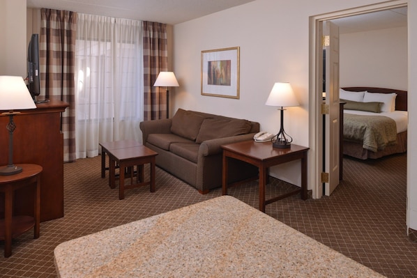 Ein Hotelzimmer mit braunem Sofa, zwei kleinen Tischen, einem Bett, einem Telefon und einem Gemälde an der Wand.