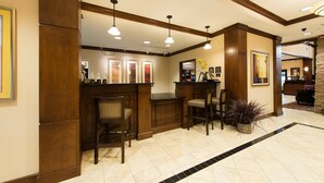 A lobby with a reception desk, two bar stools, and a potted plant. - 2 Bedroom | Free Wi-Fi + Breakfast, Gym Access (Columbia)