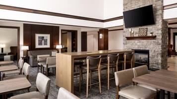 Un hall de hotel con zona de bar, asientos, chimenea y un televisor de pantalla plana montado en una pared de piedra.