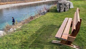 Eine Flussbank mit einer Sitzbank und einer Person beim Angeln.