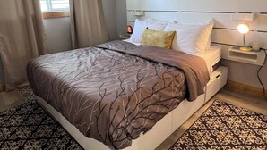 Ein ordentlich gemachtes Bett mit einer gemusterten Tagesdecke, ein Nachttisch mit einer Lampe und ein gemusterter Teppich auf dem Boden.