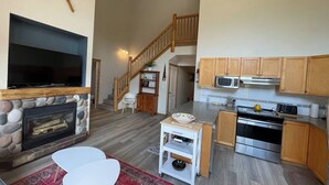 Ein geräumiger Wohnbereich mit Kamin aus Stein, einem Flachbildfernseher und einer Treppe, die in einen oberen Bereich führt.