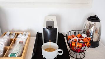 Una macchina per il caffè, una tazza di caffè, un cesto di bicchieri arancioni e una scatola di capsule di caffè su un tavolo.